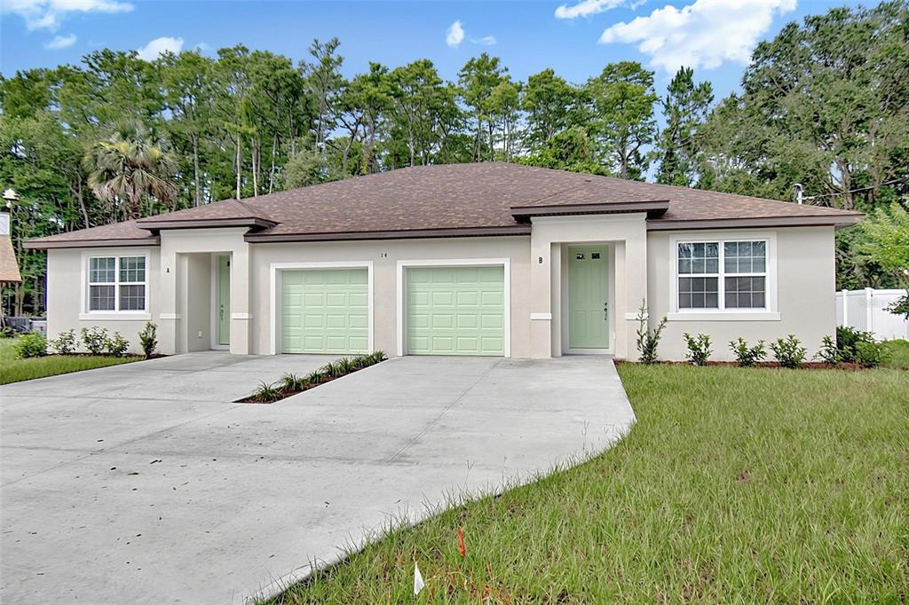 A single-story duplex with light-colored stucco, two garage doors, and a brown shingled roof — 14 ULLYNN PLACE UNIT B, PALM COAST, FL