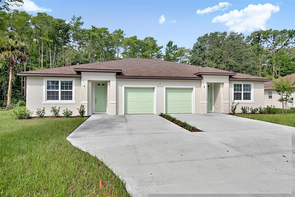 A single-story duplex with light-colored stucco, green garage doors, and a concrete driveway — 14 ULLYNN PLACE UNIT B, PALM COAST, FL