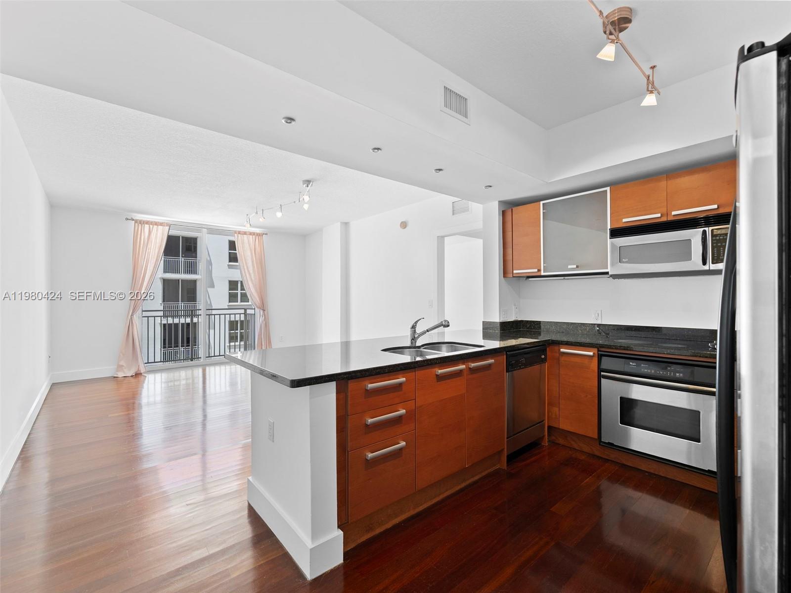 A kitchen with wood cabinets and granite countertops overlooks a living area with balcony access — 2030 S Douglas Rd # 610, Coral Gables FL 33134, CORAL GABLES, FL