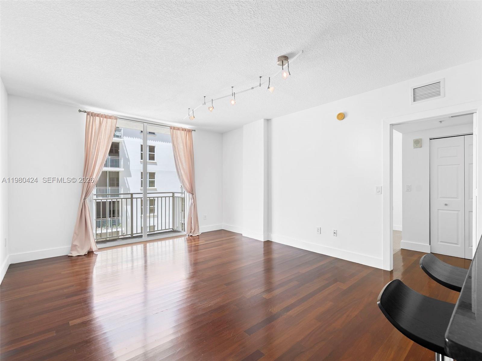 A bright living room features dark hardwood floors, white walls, and a sliding glass balcony door — 2030 S Douglas Rd # 610, Coral Gables FL 33134, CORAL GABLES, FL