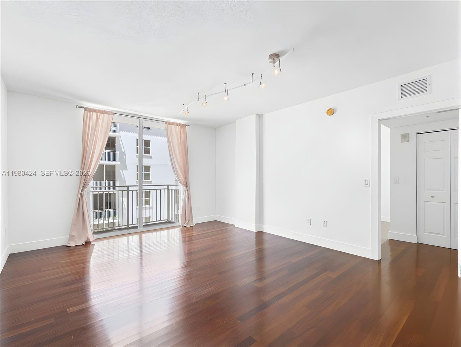 An empty room features dark hardwood floors, white walls, track lighting, and a balcony door — 2030 S Douglas Rd # 610, Coral Gables FL 33134, CORAL GABLES, FL