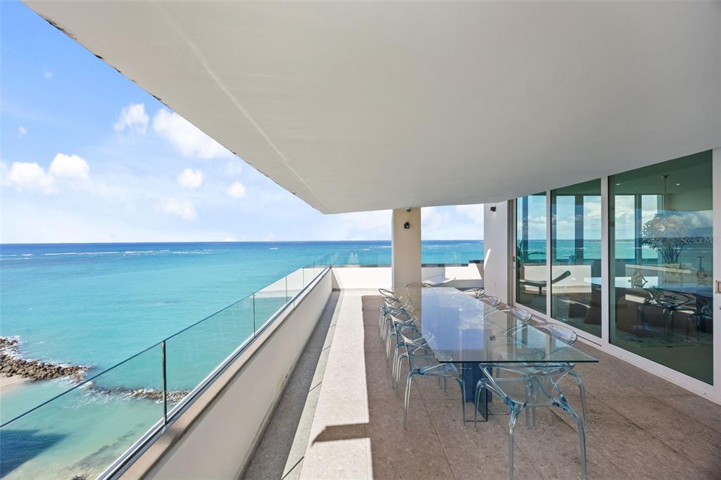 A balcony with a glass dining table and chairs overlooks the ocean — 3307 AVE ISLA VERDE UNIT PH, CAROLINA, PR