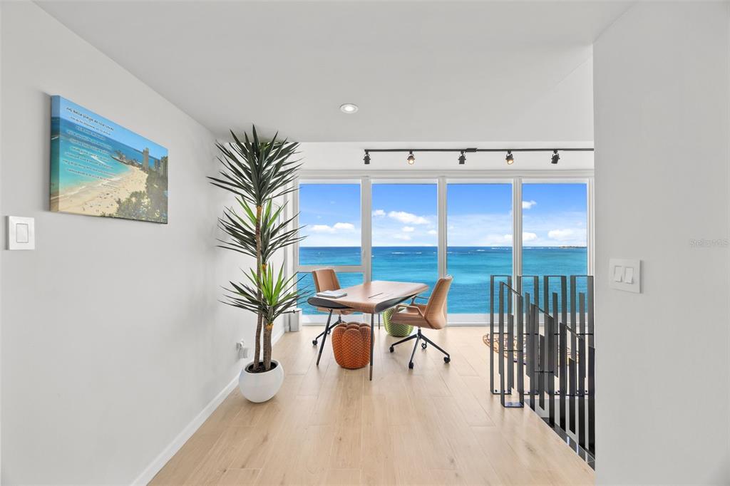 A modern home office features a wooden desk, two chairs, and floor-to-ceiling ocean views — 3307 AVE ISLA VERDE UNIT PH, CAROLINA, PR
