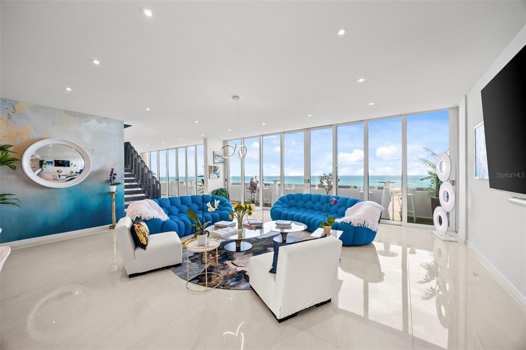 A living room features blue tufted sofas, white armchairs, and floor-to-ceiling windows overlooking the ocean — 3307 AVE ISLA VERDE UNIT PH, CAROLINA, PR
