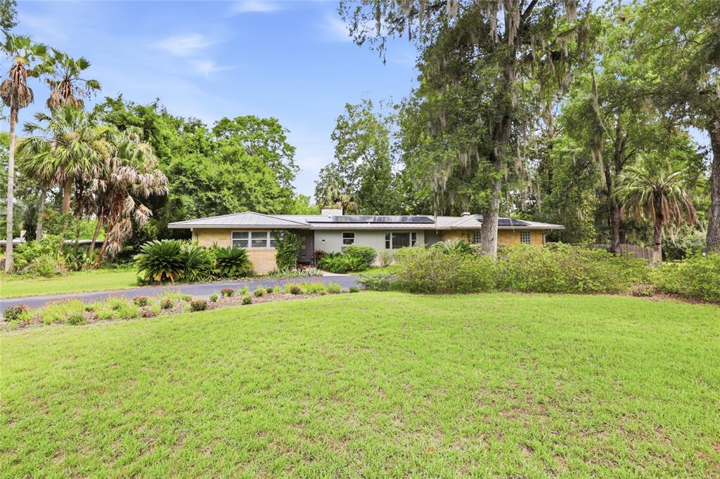 A single-story house with a metal roof and solar panels sits on a grassy lot — 2006 NW 14TH AVENUE, GAINESVILLE, FL