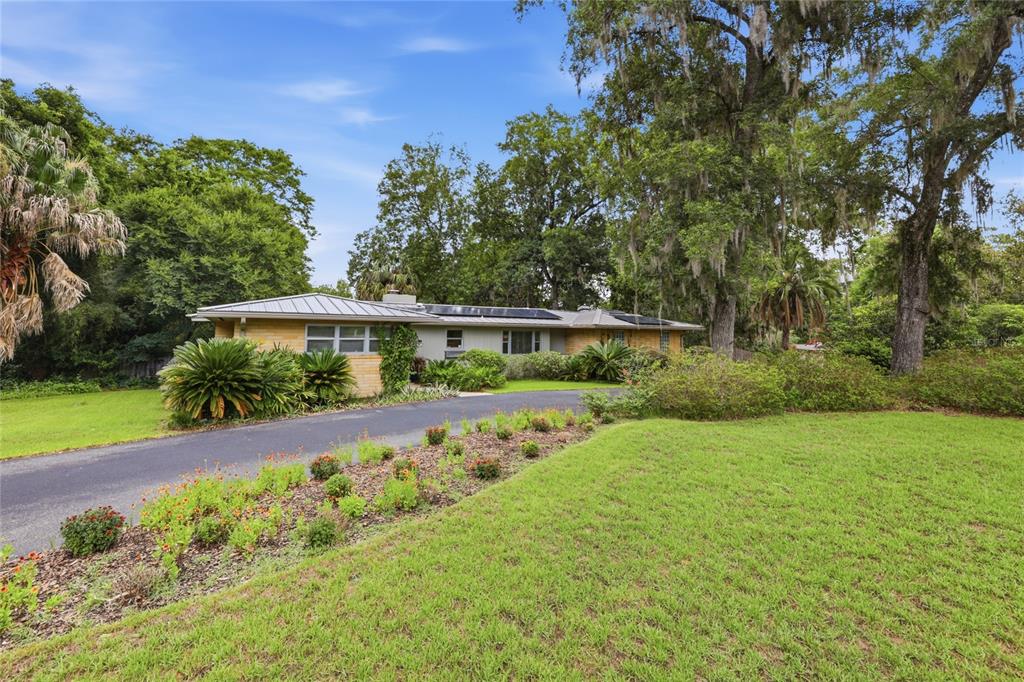 A single-story house with a metal roof sits behind a curved driveway and landscaped lawn — 2006 NW 14TH AVENUE, GAINESVILLE, FL