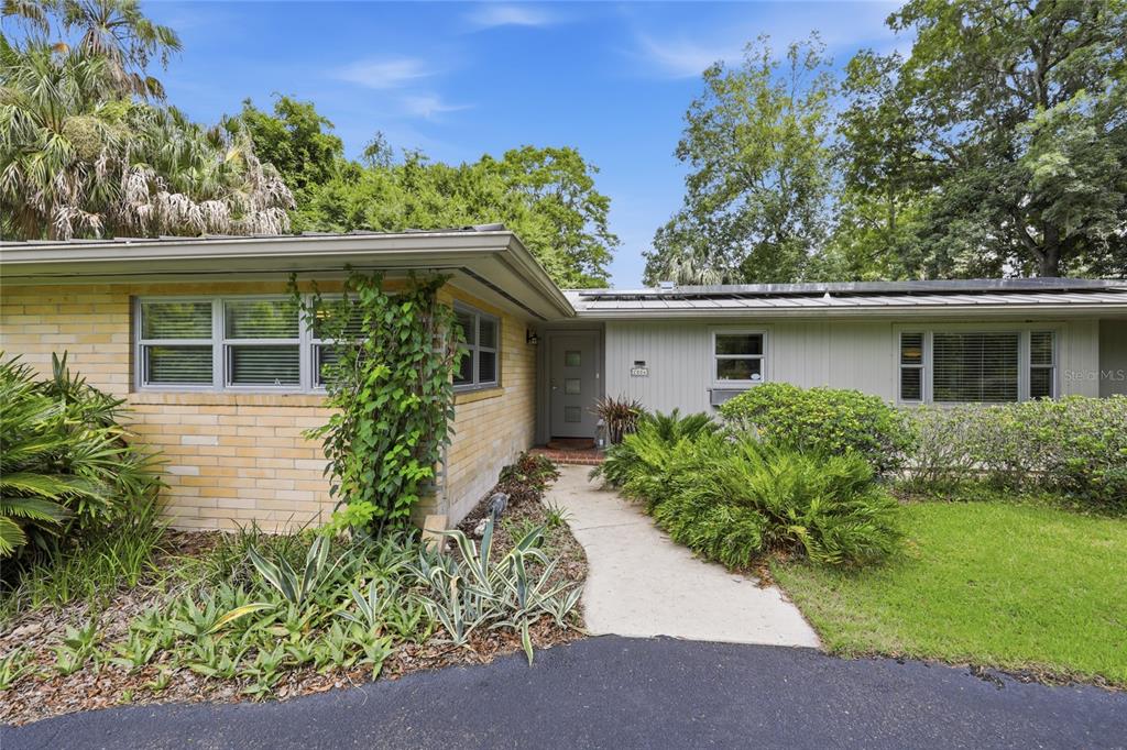 A single-story house features a yellow brick facade, a gray front door, and a concrete walkway — 2006 NW 14TH AVENUE, GAINESVILLE, FL