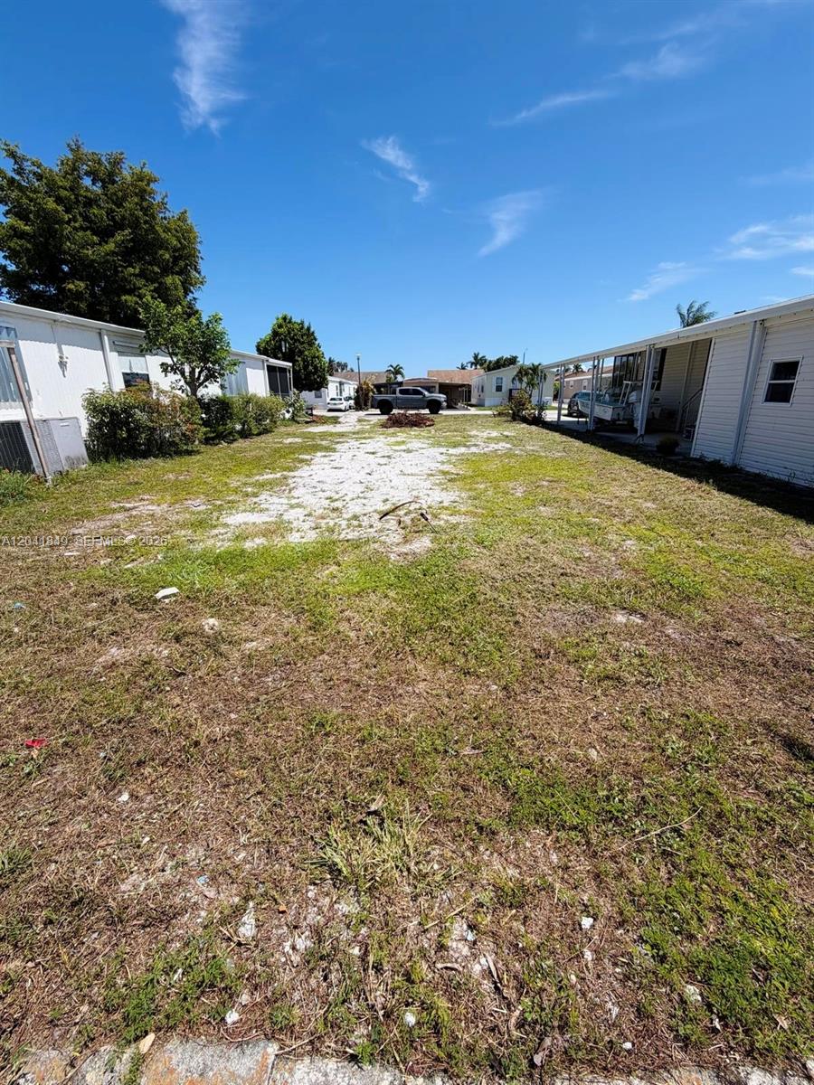 A narrow, grassy lot sits between two mobile homes under a clear blue sky — 2651 E Marina Dr, Dania Beach FL 33312, DANIA BEACH, FL