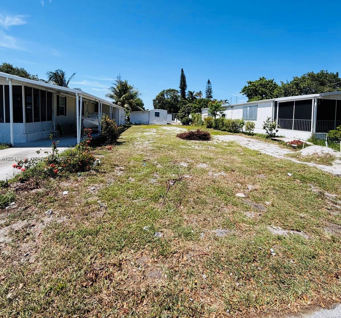 A grassy lot sits between two manufactured homes under a clear blue sky — 2651 E Marina Dr, Dania Beach FL 33312, DANIA BEACH, FL