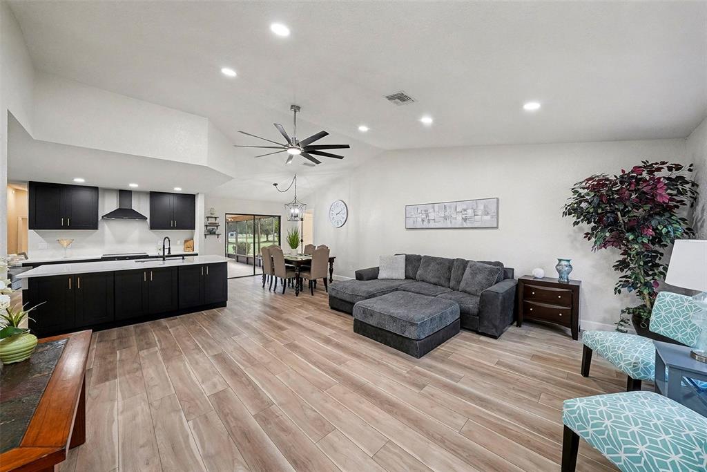 An open-concept living room and kitchen feature dark cabinetry, wood-look flooring, and a sectional sofa — 11325 GLENMONT DRIVE, TAMPA, FL