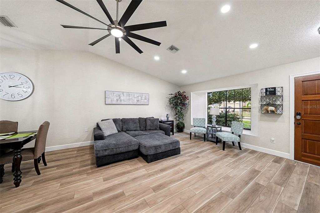 A living room features a gray sectional sofa, wood-look flooring, and a large ceiling fan — 11325 GLENMONT DRIVE, TAMPA, FL