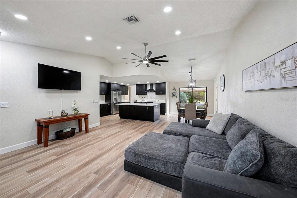 An open-concept living room and kitchen feature light wood flooring and dark cabinetry — 11325 GLENMONT DRIVE, TAMPA, FL