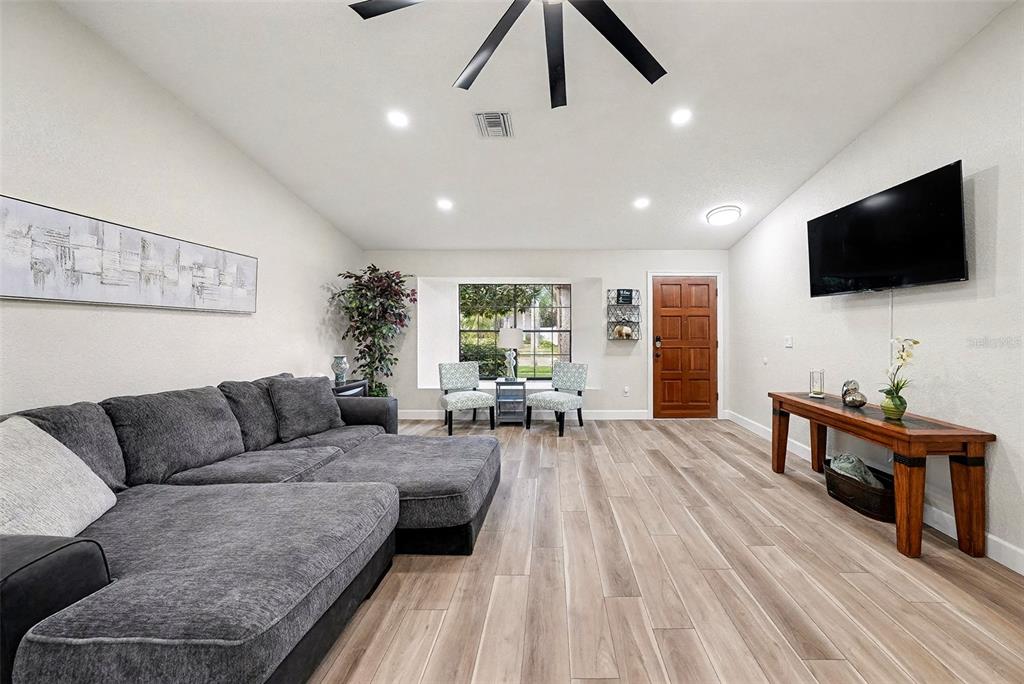 A living room features a gray sectional sofa, wood-look flooring, and a wall-mounted television — 11325 GLENMONT DRIVE, TAMPA, FL