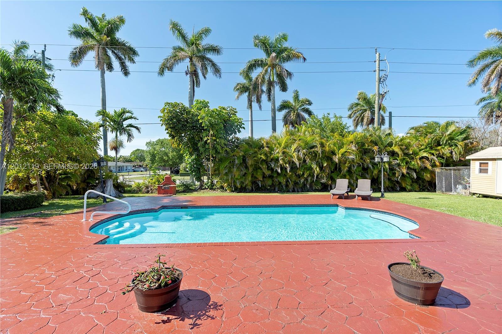 A backyard features a swimming pool with a red patio, palm trees, and lounge chairs — 8895 SW 184th Ter, Cutler Bay FL 33157, CUTLER BAY, FL