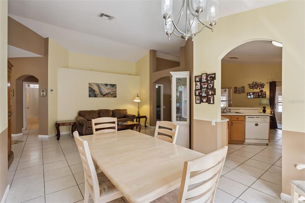 A dining area with a light wood table and chairs opens into a living room — 3136 CRANES COVE LOOP, KISSIMMEE, FL