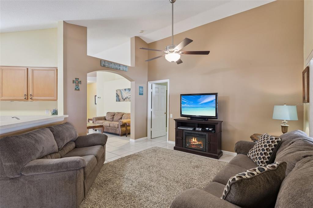 A living room with beige walls, brown sofas, a fireplace media console, and a ceiling fan — 3136 CRANES COVE LOOP, KISSIMMEE, FL