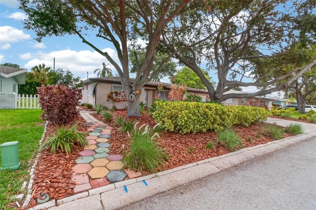 A single-story house with a colorful hexagonal paver walkway and large trees in the front yard — 2012 RIPON DRIVE, CLEARWATER, FL