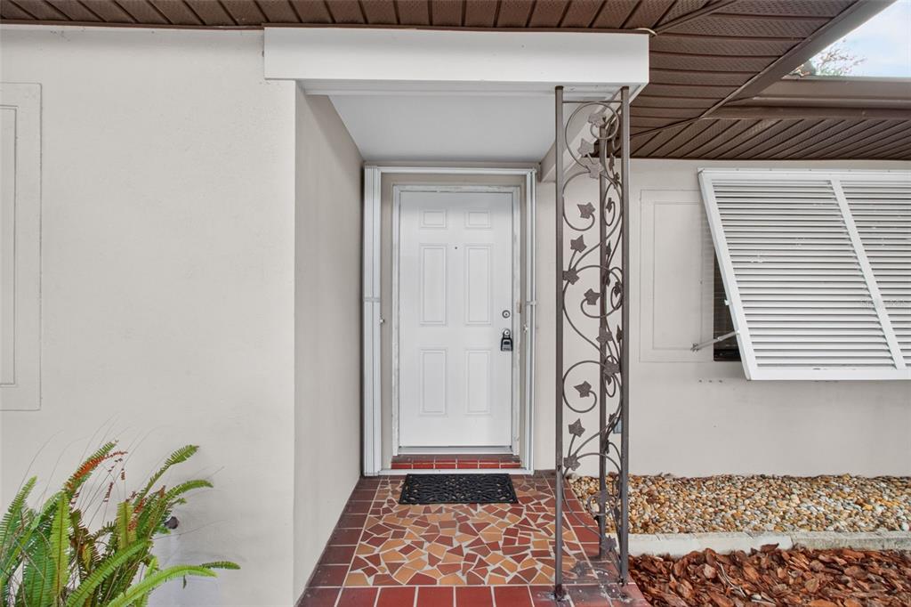 A white front door with a decorative metal support column and tiled entryway — 2012 RIPON DRIVE, CLEARWATER, FL