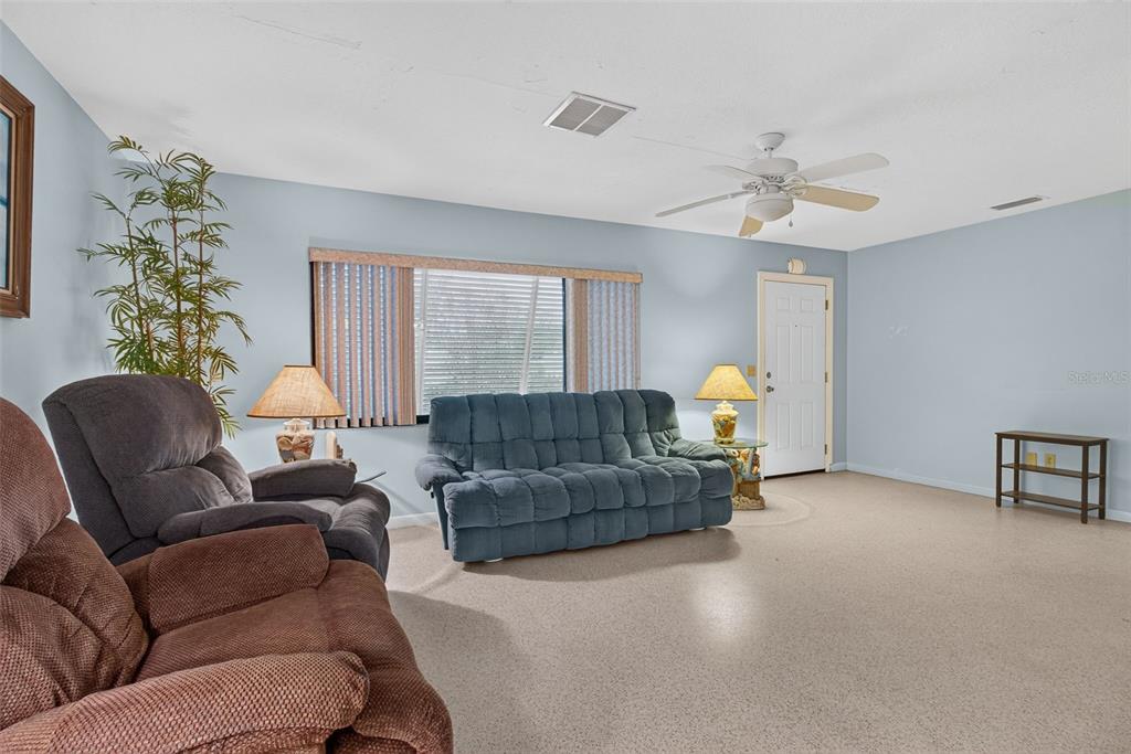 A living room features a blue sofa, two recliners, a ceiling fan, and carpeted floors — 2012 RIPON DRIVE, CLEARWATER, FL