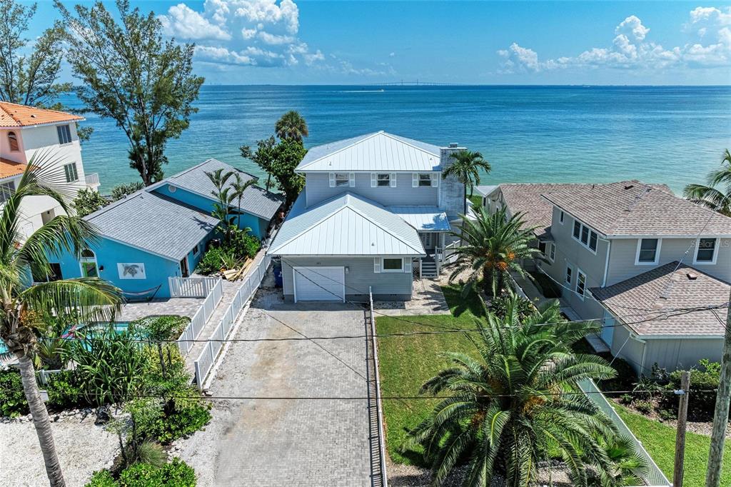 An aerial view shows a two-story gray house with a metal roof near the ocean — 893 N SHORE DRIVE, ANNA MARIA, FL