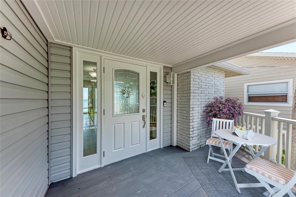 A covered front porch features a white door with glass panels, gray siding, and seating — 893 N SHORE DRIVE, ANNA MARIA, FL