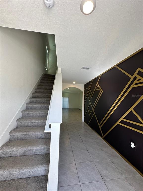 A staircase with gray carpet sits beside a wall featuring a black and gold geometric design — 5703 HOLLINGWORTH TRAIL, WESLEY CHAPEL, FL