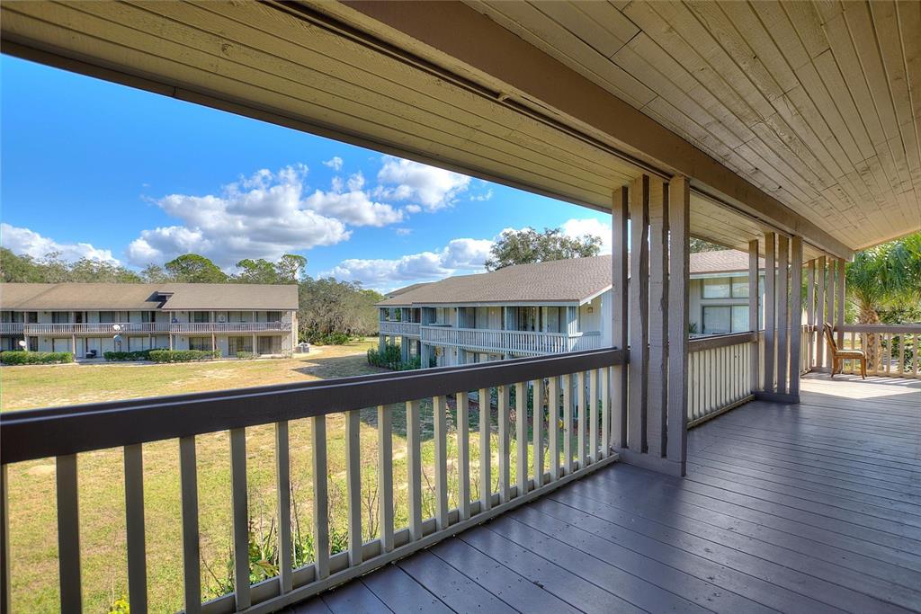 A covered wooden balcony overlooks a grassy courtyard and neighboring apartment buildings — 907 TENNIS WAY UNIT 3147/8, HAINES CITY, FL