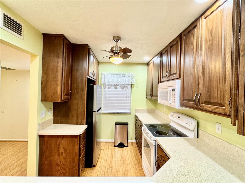 A galley kitchen features wood cabinets, light countertops, a white stove, and a ceiling fan — 7 MOSER COURT N, HOMOSASSA, FL