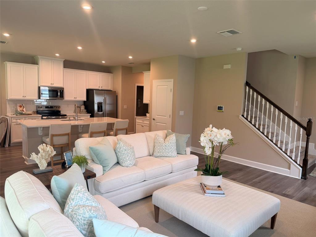 An open-concept living room and kitchen featuring white cabinetry, a kitchen island, and stairs — 1291 RIBBON PLACE, PALM COAST, FL