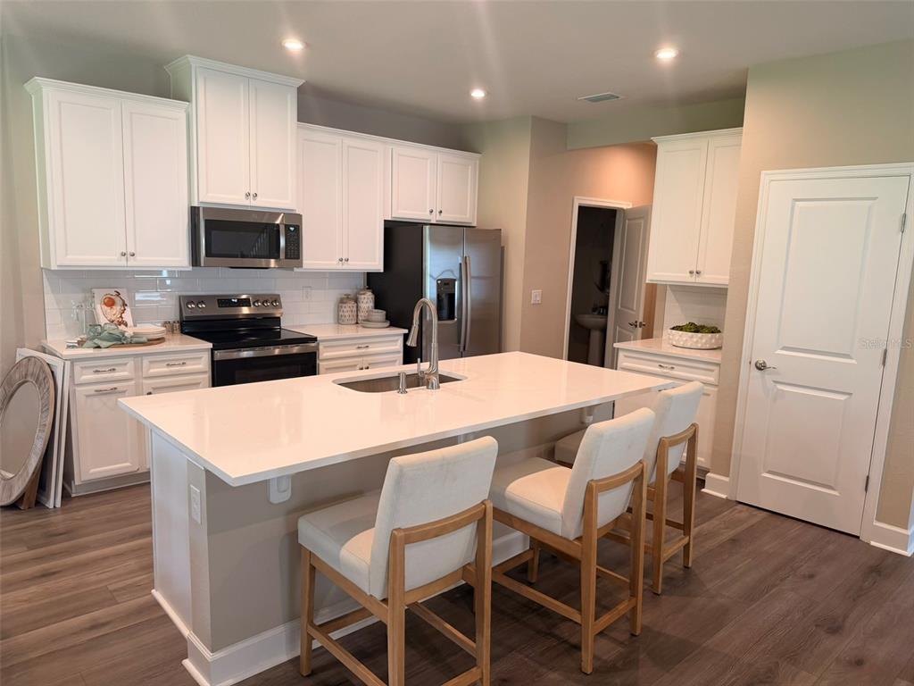 A modern kitchen features white cabinets, a central island with a sink, and wood flooring — 1291 RIBBON PLACE, PALM COAST, FL