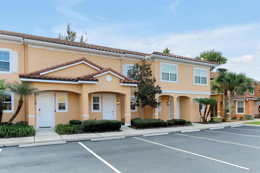 A two-story tan stucco townhouse with a tiled roof and a parking lot in front — 2691 CORVETTE LANE, KISSIMMEE, FL
