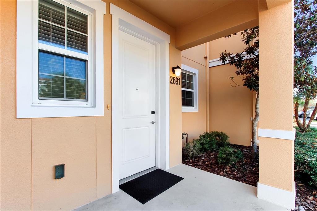 A white front door with a house number sits on a covered concrete porch — 2691 CORVETTE LANE, KISSIMMEE, FL