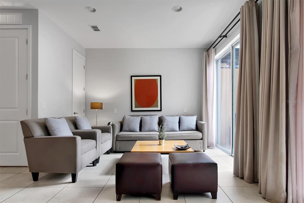 A living room features a gray sofa, matching armchair, two leather ottomans, and a coffee table — 2691 CORVETTE LANE, KISSIMMEE, FL