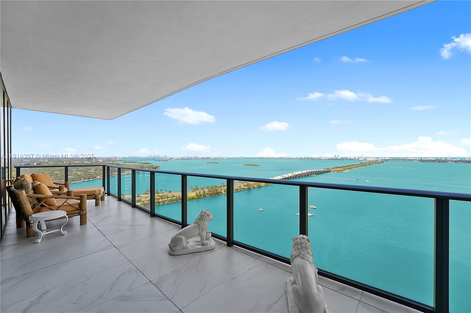 A balcony with marble flooring, outdoor seating, and two lion statues overlooks a bay — 3131 NE 7th Ave # 3106, Miami FL 33137, MIAMI, FL