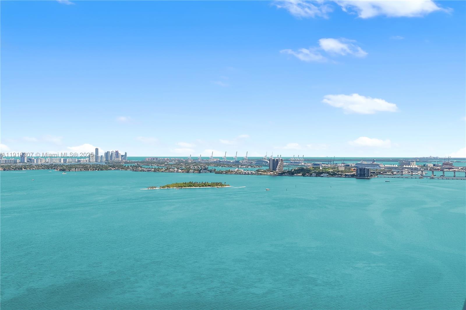 An elevated view of Biscayne Bay featuring a small island, distant city skyline, and cranes — 3131 NE 7th Ave # 3106, Miami FL 33137, MIAMI, FL