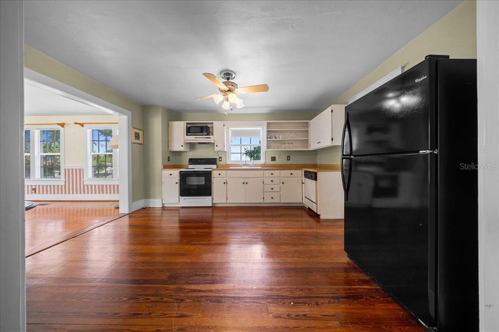 A kitchen with white cabinets, a black refrigerator, and hardwood floors opens to another room — 319 CARNATION COURT, APOPKA, FL