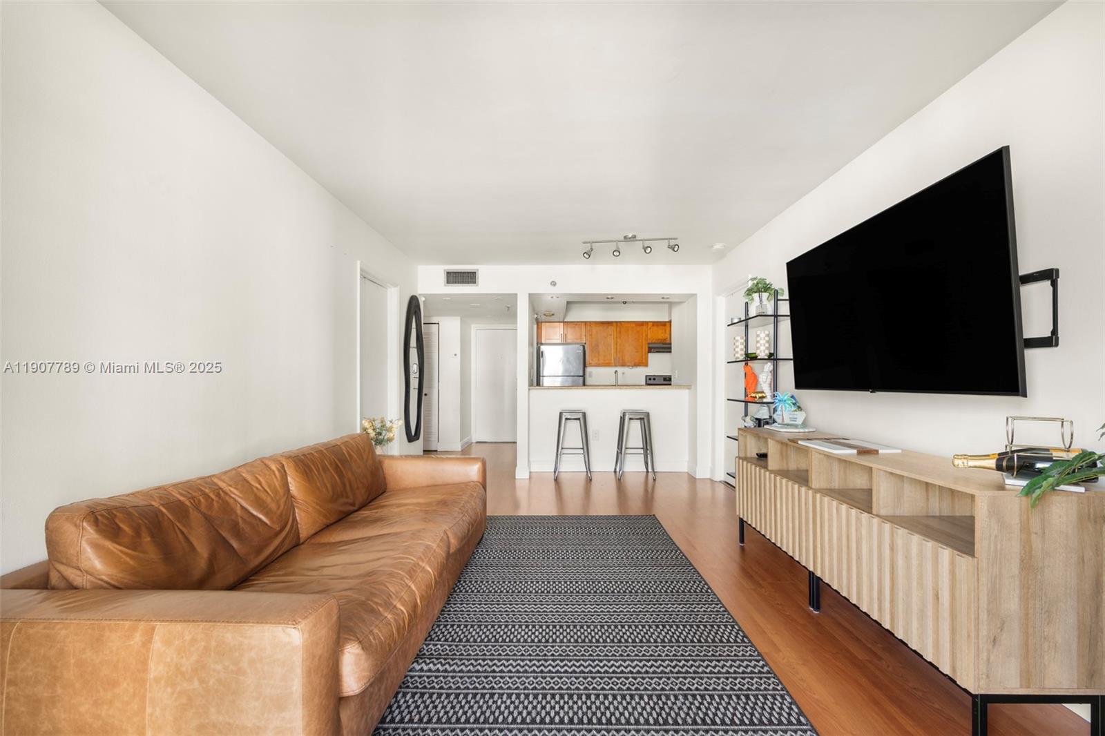 A living room features a brown leather sofa, a patterned rug, and a wall-mounted television — 850 N Miami Ave # 906, Miami FL 33136, MIAMI, FL