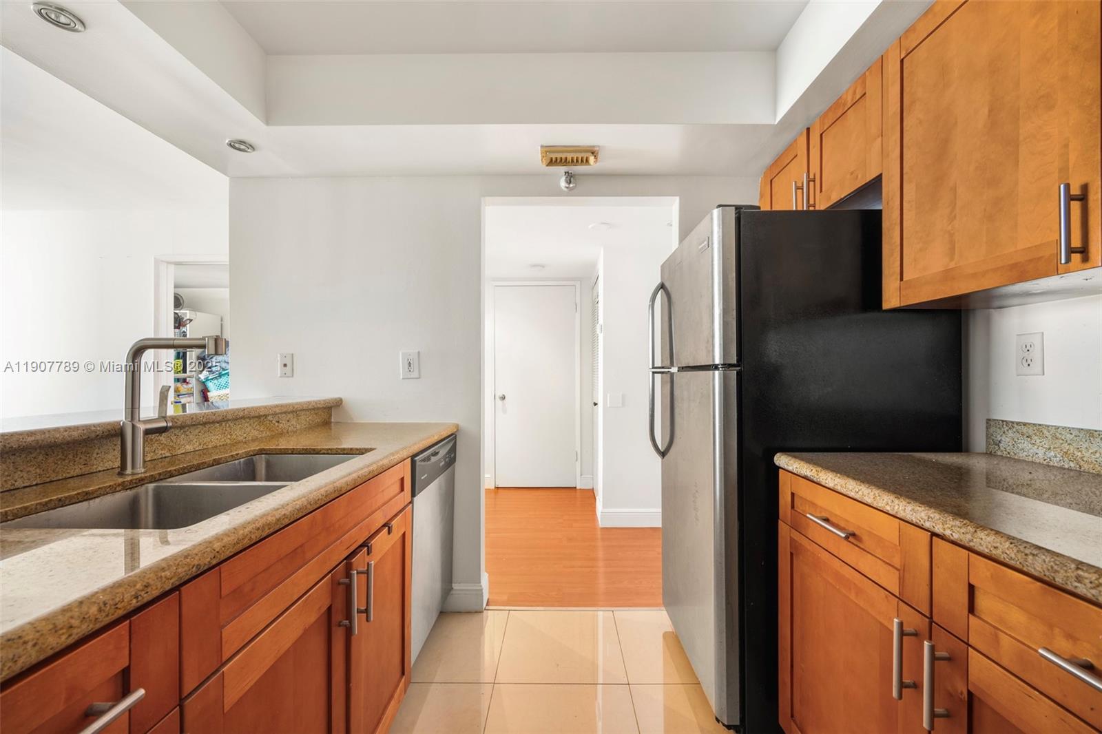 A kitchen features wooden cabinets, granite countertops, a stainless steel refrigerator, and tile flooring — 850 N Miami Ave # 906, Miami FL 33136, MIAMI, FL