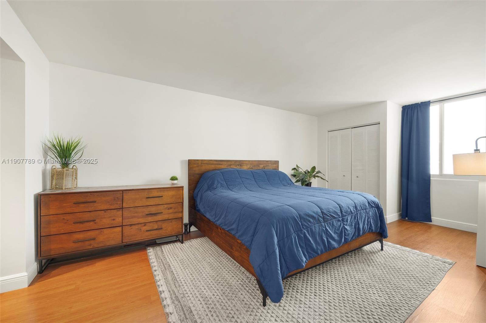 A bedroom features a wooden bed frame, a matching dresser, and a blue comforter — 850 N Miami Ave # 906, Miami FL 33136, MIAMI, FL