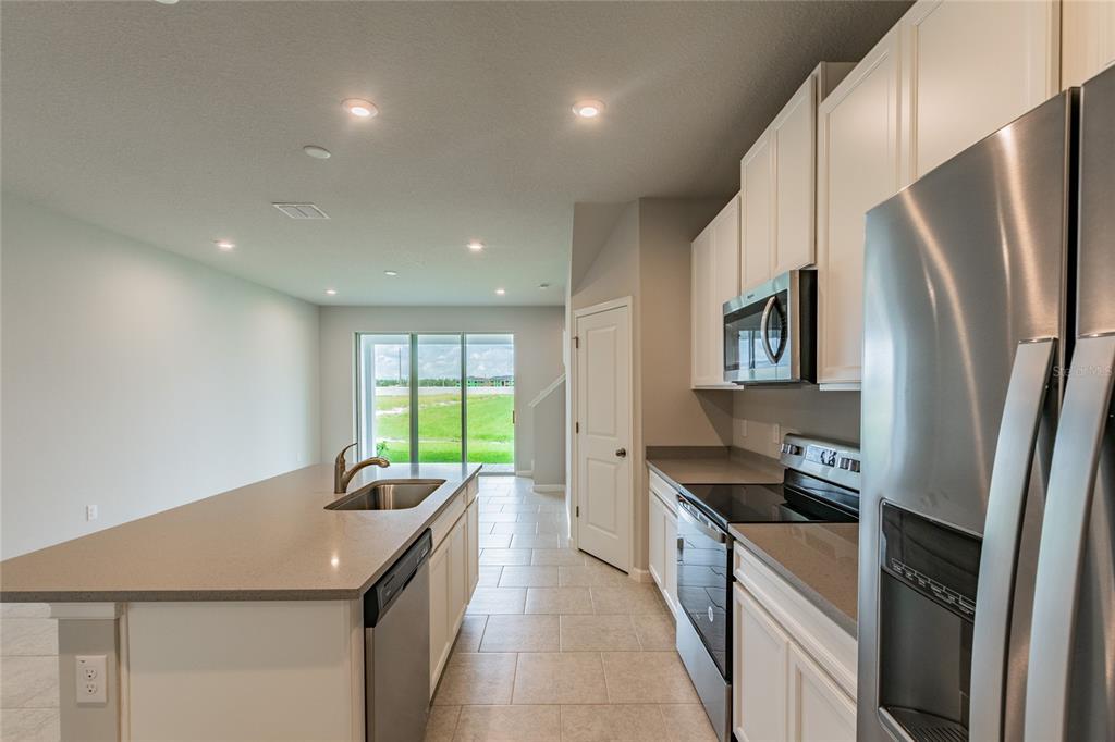 A modern kitchen features white cabinets, stainless steel appliances, and a central island with sink — 19309 BLUE POND DRIVE, LUTZ, FL