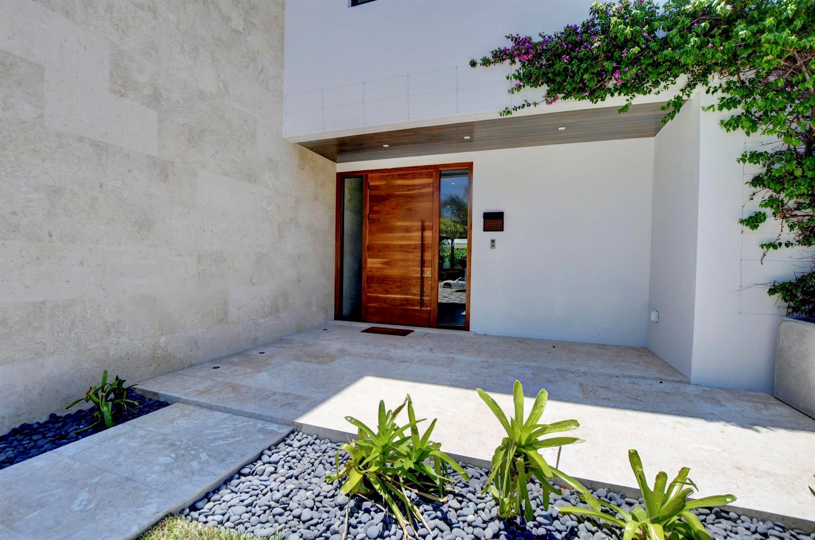 A modern home entrance features a wooden door, stone flooring, and a bougainvillea-covered wall — 855 NW 4th Avenue, Boca Raton FL 33432, BOCA RATON, FL