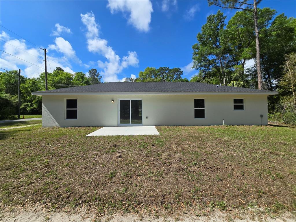 The rear exterior of a single-story house features a concrete patio and sliding glass doors — 131 FISHER ROAD, OCKLAWAHA, FL