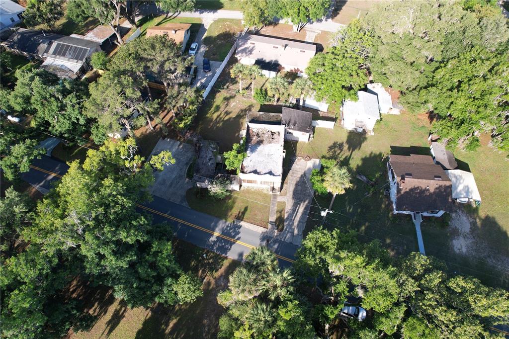 Aerial view of a residential property featuring a fire-damaged house and surrounding wooded lots — 6405 SUNNYSIDE DRIVE, LEESBURG, FL