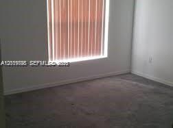 An empty room with gray carpeting, white walls, and vertical blinds covering a window — OTHER CITY - IN THE STATE OF FLORIDA, FL