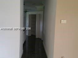 A narrow hallway with dark flooring leads toward an open doorway and a kitchen area — OTHER CITY - IN THE STATE OF FLORIDA, FL