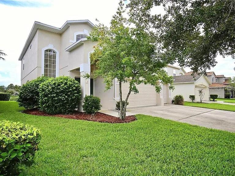 A two-story house with a beige exterior, a green lawn, and a concrete driveway — 14802 YORKSHIRE RUN DRIVE, ORLANDO, FL