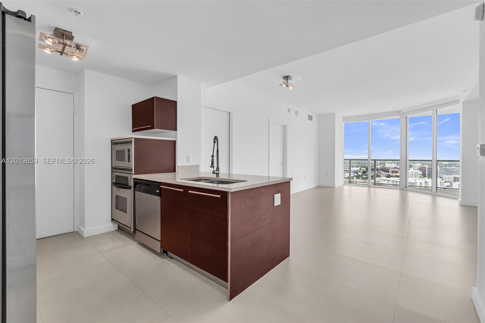A modern kitchen with dark wood cabinets and stainless steel appliances opens to a living area — 1900 N Bayshore Dr # 3216, Miami FL 33132, MIAMI, FL