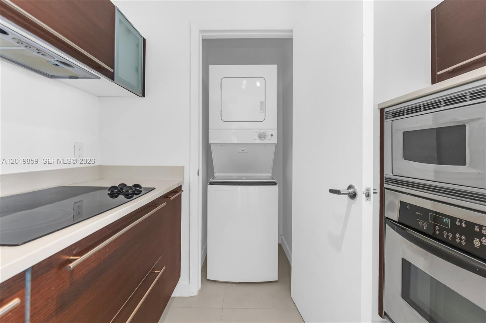 A kitchen features dark wood cabinets, a black cooktop, and a stacked laundry unit — 1900 N Bayshore Dr # 3216, Miami FL 33132, MIAMI, FL