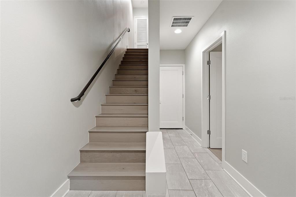 A staircase with light wood steps and a black handrail sits beside a tiled hallway — 2511 N GRADY AVENUE UNIT 89, TAMPA, FL