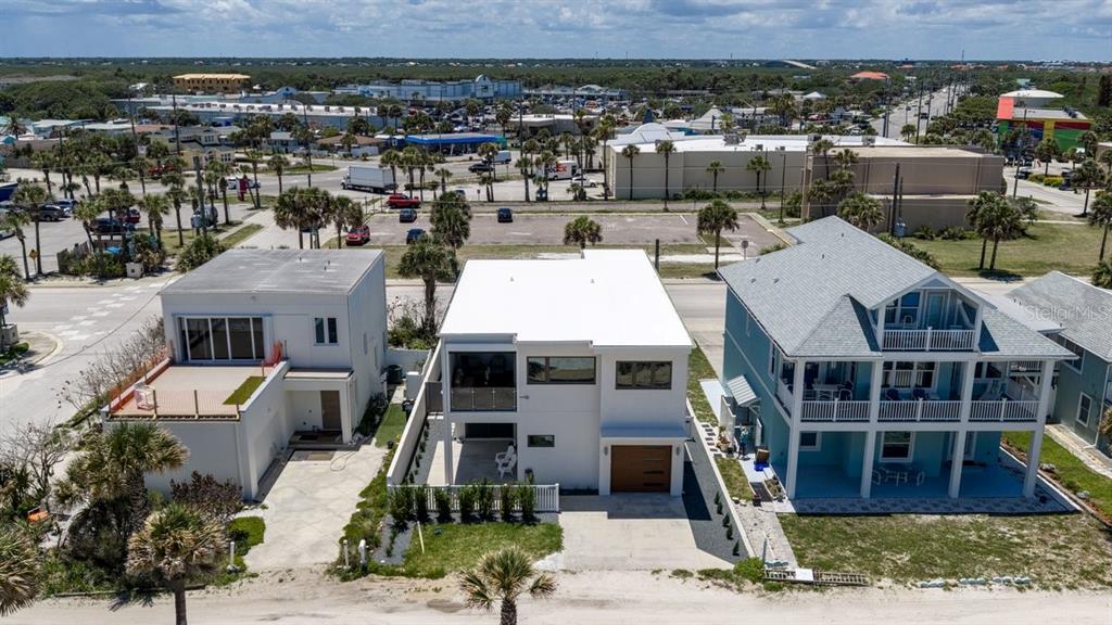 An aerial view shows three coastal houses situated along a road near a parking lot — 1309 S ATLANTIC AVENUE, NEW SMYRNA BEACH, FL
